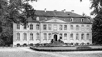 Historisches Herrenhaus umgeben von Bäumen, mit einer eleganten Fassade und einem gepflegten Garten im Vordergrund.