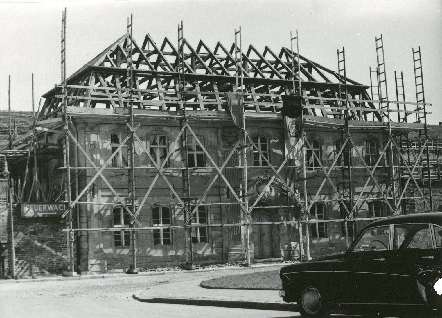 Kleist-Gedenk- und Forschungsstätte 1967 ©Kleist-Museum Schwarz-Weiß-Foto der Kleist-Gedenk und Forschungsstätte im Umbau 1967; ehemalige Garnisonschule, die komplett mit Baugerüst ummantelt ist; im Vordergrund recht sieht man die Motorhaube eines großen PKWs, am Gebäude hängt eine DDR-Flagge mit Hammer, Zirkel und Ehrekranz-Emblem