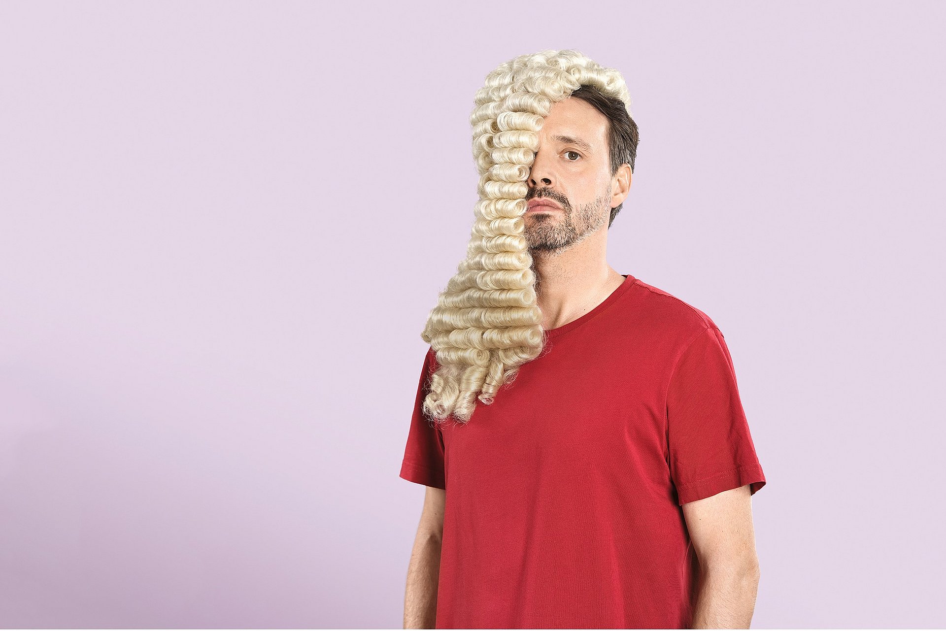 Schauspieler in rotem T-Shirt mit Perücke, über sein halbes Gesicht gehängt