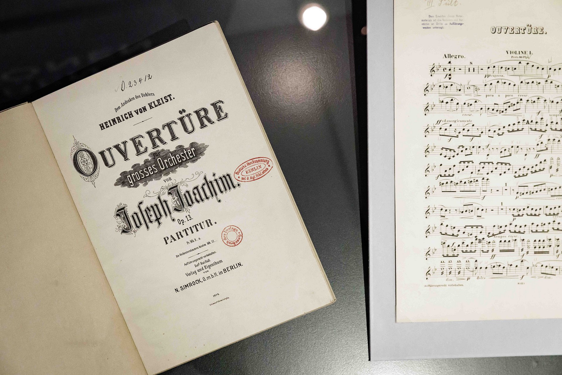 Offenes Buch, das links die Titelseite von „Ouverture“ von Joseph Joachim und rechts Notenblätter zeigt. Die Szene vermittelt einen historischen und künstlerischen Eindruck.