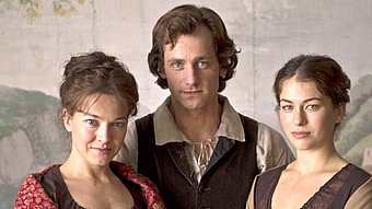 Drei Personen in historischer Kleidung posieren vor einer malerischen Kulisse, die eine romantische Atmosphäre vermittelt.