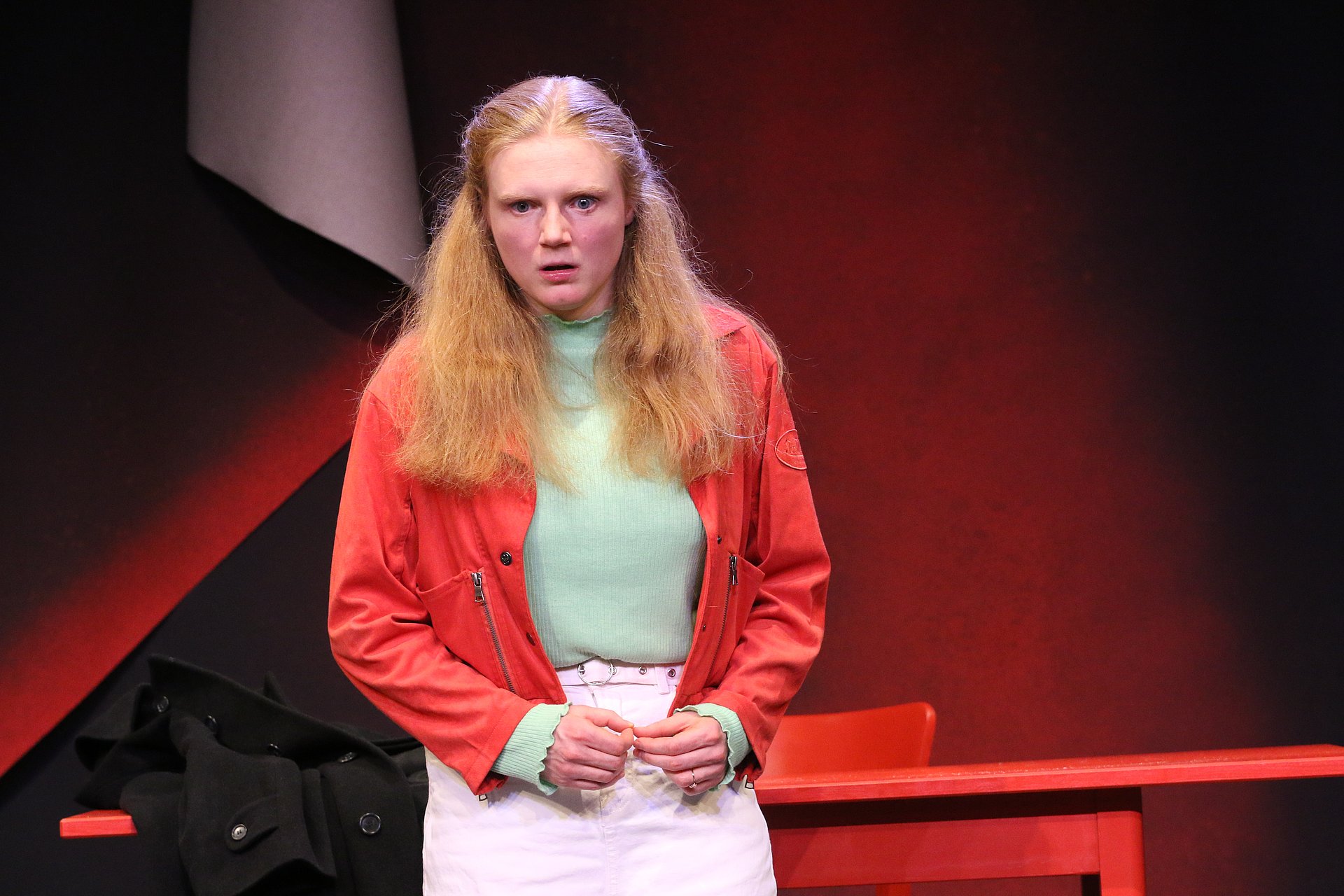 Schauspielerin als Eve vor rotem Tisch und rotschwarzem Hintergrund