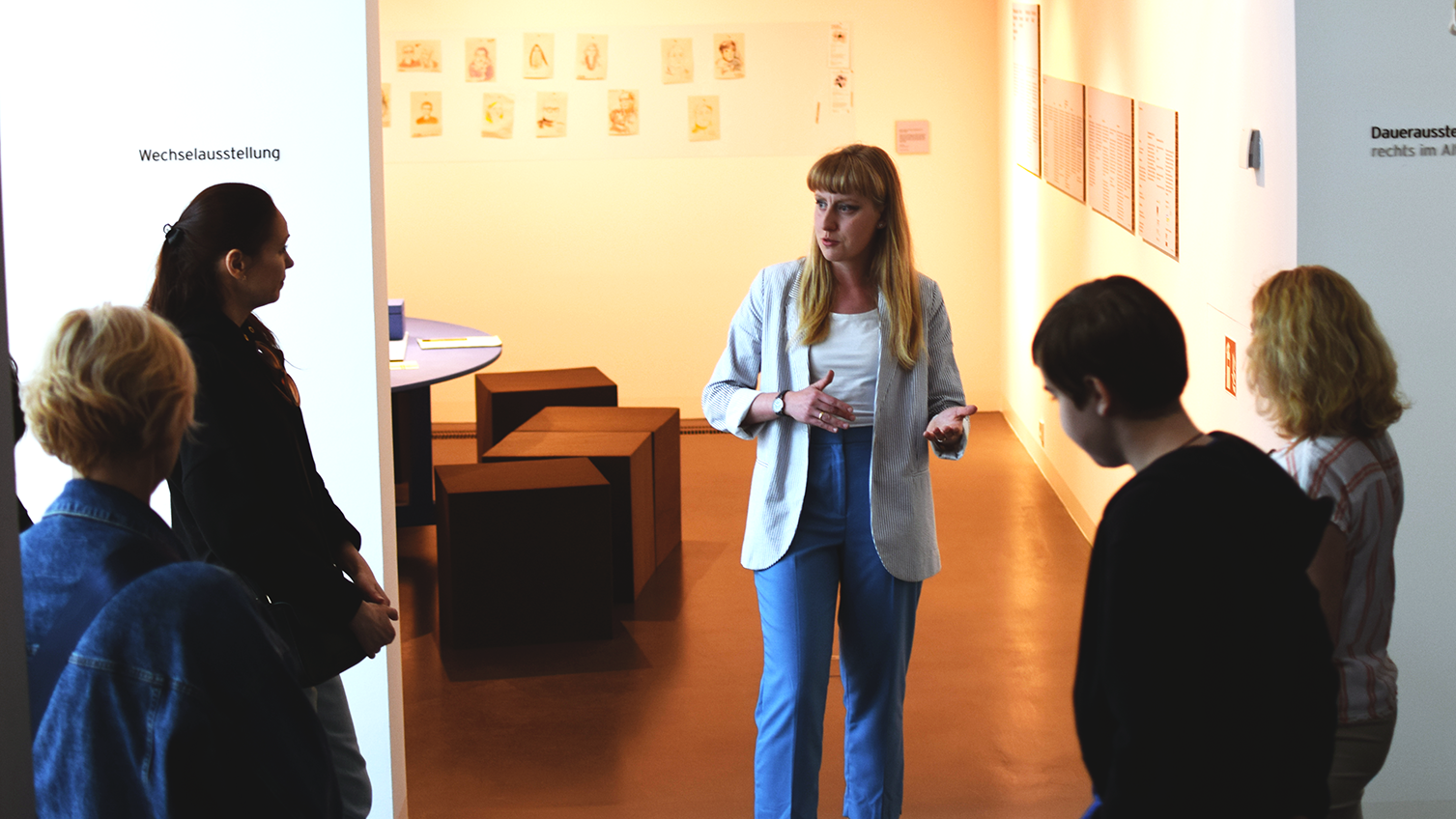 Führung durch das Kleist-Museum auf Ukrainisch im Durchgang zwischen Sonder- und Dauerausstellung; Führungsreferentin mit langer blauer Hose, weißem T-Shirt und hellblauem Blazer und langen blonden Haar von vorne, mehrere Teilnehmer*innen von hinten zu sehen