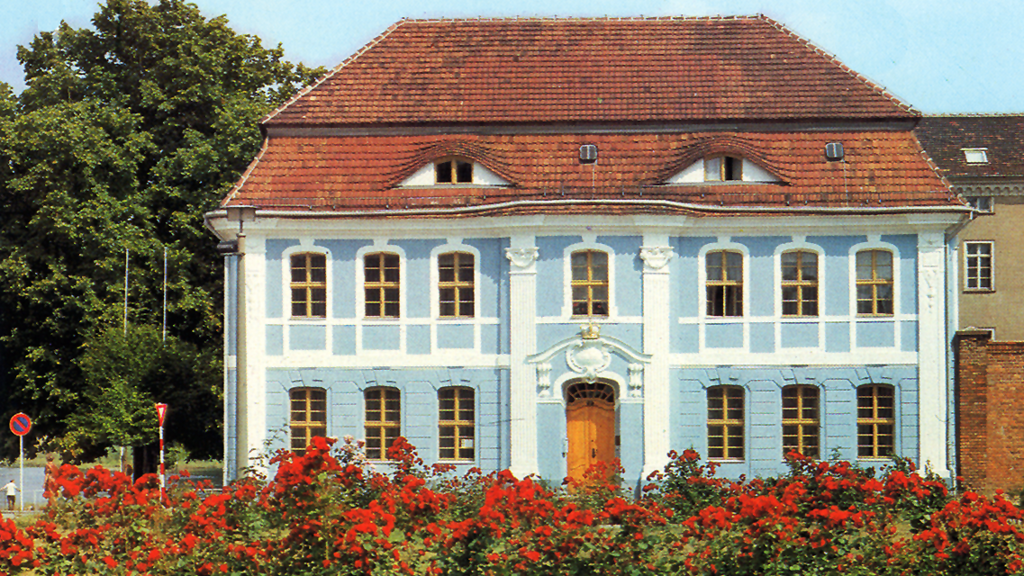 Kleist-Museum im Jahr 1982 mit hellblauer Fassade, weißem Stuck und rotem Dach; im Vordergrund Rosenbüsche mit vielen roten Rosenblüten, links im Hintergrund ein stark belaubter Baum